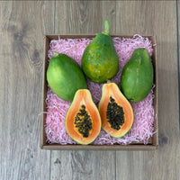 Thumbnail for Tropical Fruit Box Golden Papaya, 3 lbs. Two whole green papayas and one halved to show vibrant orange flesh and black seeds, nestled in pink crinkle paper.
