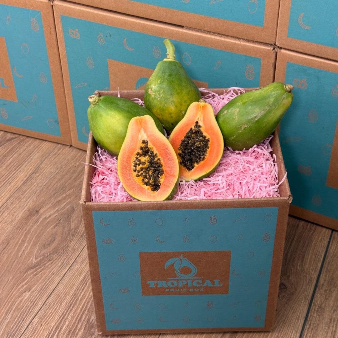 Tropical Fruit Box Golden Papaya, one cut in half showing vibrant orange flesh and black seeds, surrounded by whole green papayas.