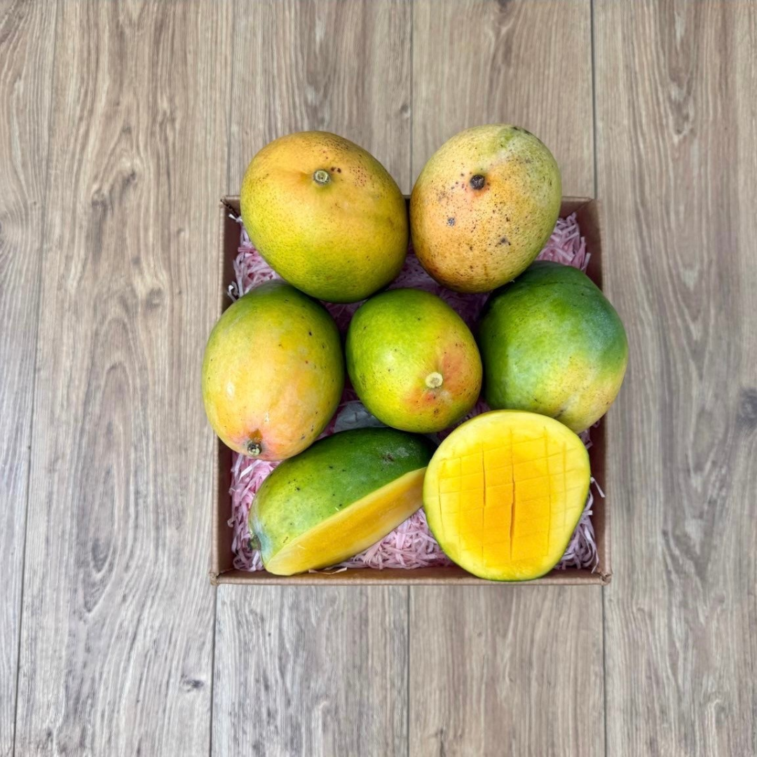 Tropical Fruit Box Kent mangoes with greenish-yellow skin and one sliced open to reveal juicy orange flesh in a box