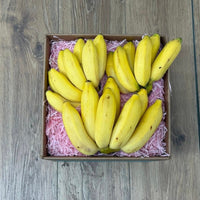Thumbnail for Tropical Fruit Box Manzano bananas, yellow, 3 lb box with pink filler on wooden background.