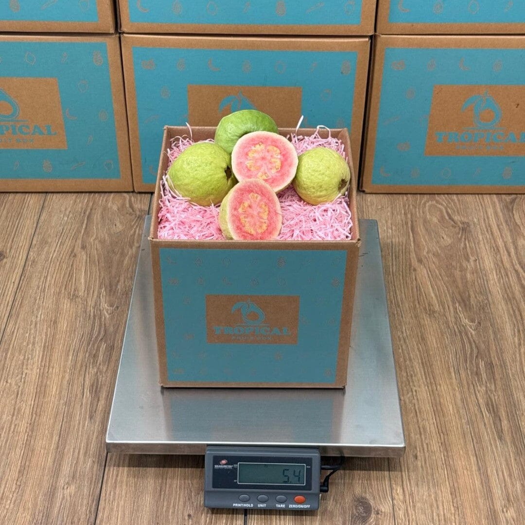 Tropical Fruit Box pink guavas, some whole and some halved, showing vibrant pink flesh and seeds, nestled in pink crinkle paper.
