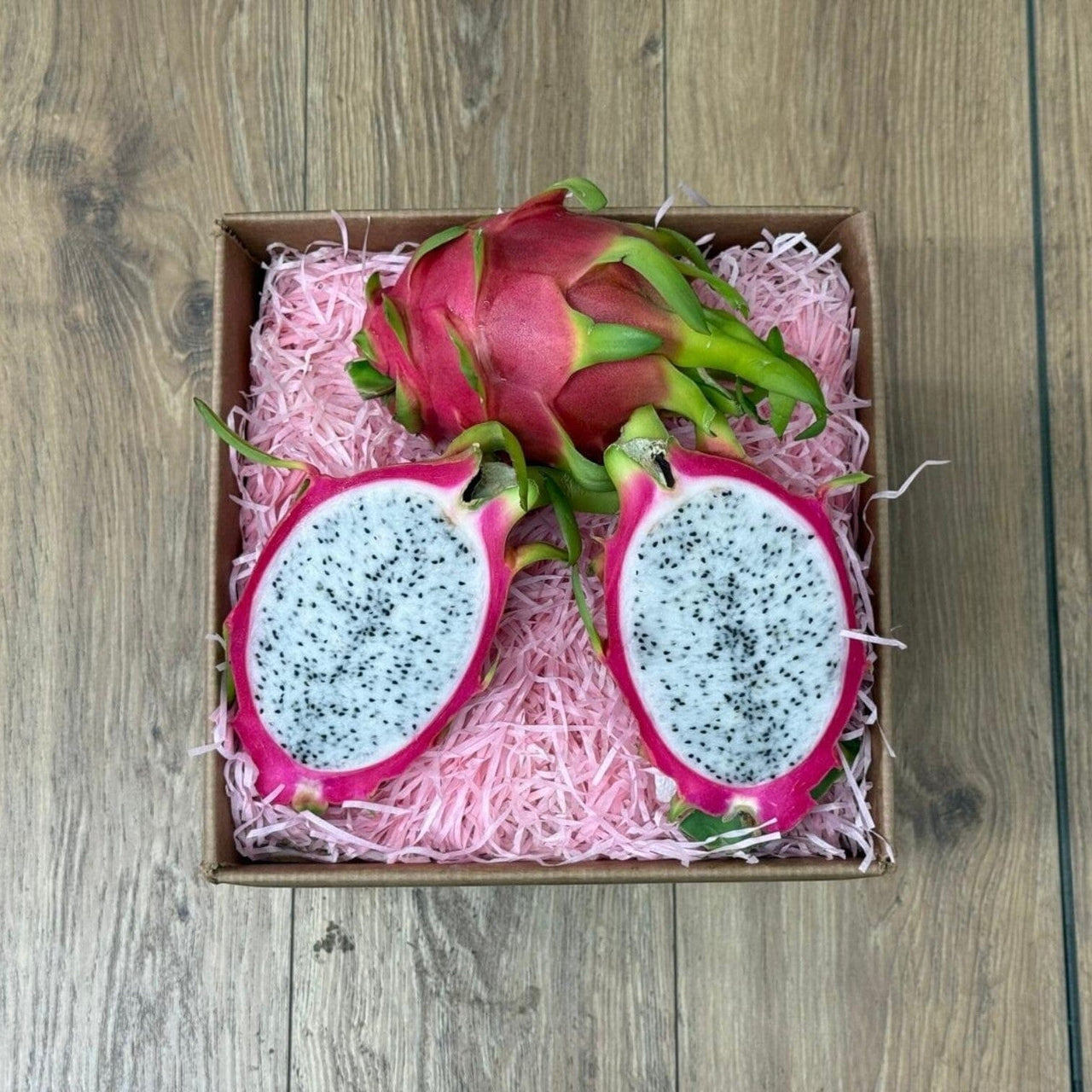 Tropical Fruit Box red dragon fruit, white flesh with black seeds, presented in a box with pink shred.