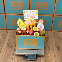 Thumbnail for Tropical Fruit Box filled with fresh pink pineapple, dragon fruit, papaya, avocado, and passion fruit on a scale.