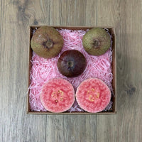 Thumbnail for Tropical Fruit Box Purple Guava: whole fruits and two halves showing vibrant pink flesh with seeds, nestled in pink shred.