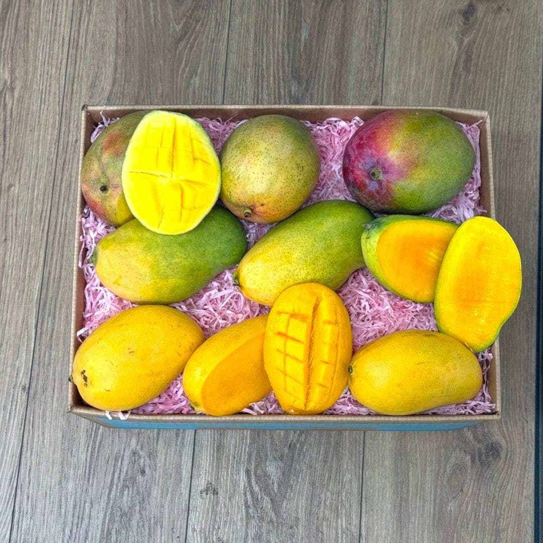 Tropical Fruit Box's assorted ripe mangoes, some whole and some sliced, in a box with pink shred.